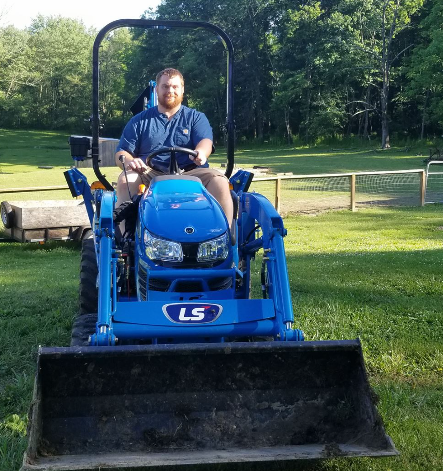 Man sitting on a blue LS tractor in a grassy field