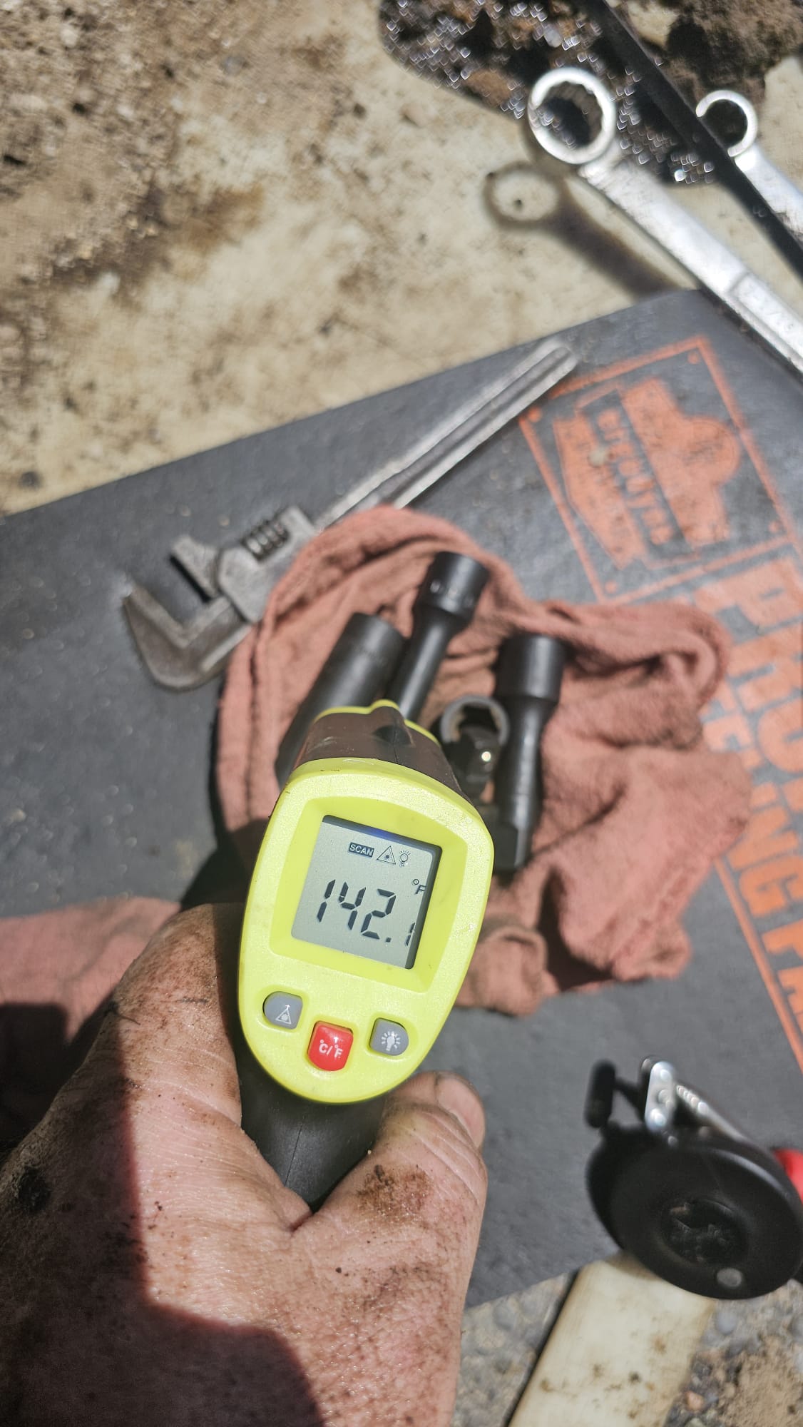 Hand holding a digital thermometer on a workbench with tools in the background on Long Island